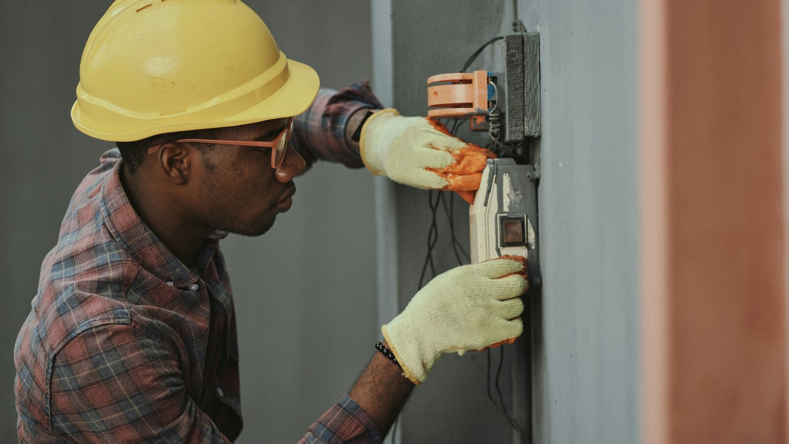 Tradesperson in a hard hat and work gloves servicing an electrical panel